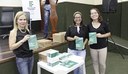 Maria do Carmo com as bolsistas Sabrina e Mayane ao lado de exemplares da Cartilha