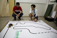 O professor Nustenil (à esquerda) e o aluno (à direita) observam robô percorrendo pista. Eles pesquisam as técnicas de controle aplicadas em robô seguidor de linha (Crédito: Anderson Lima)